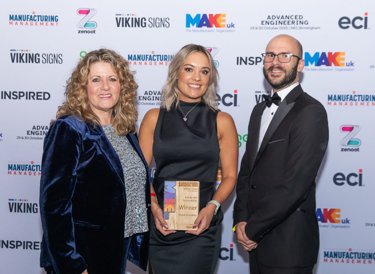 Two women and one man in evening attire standing against backdrop of logos, smiling at camera, as though receiving an award