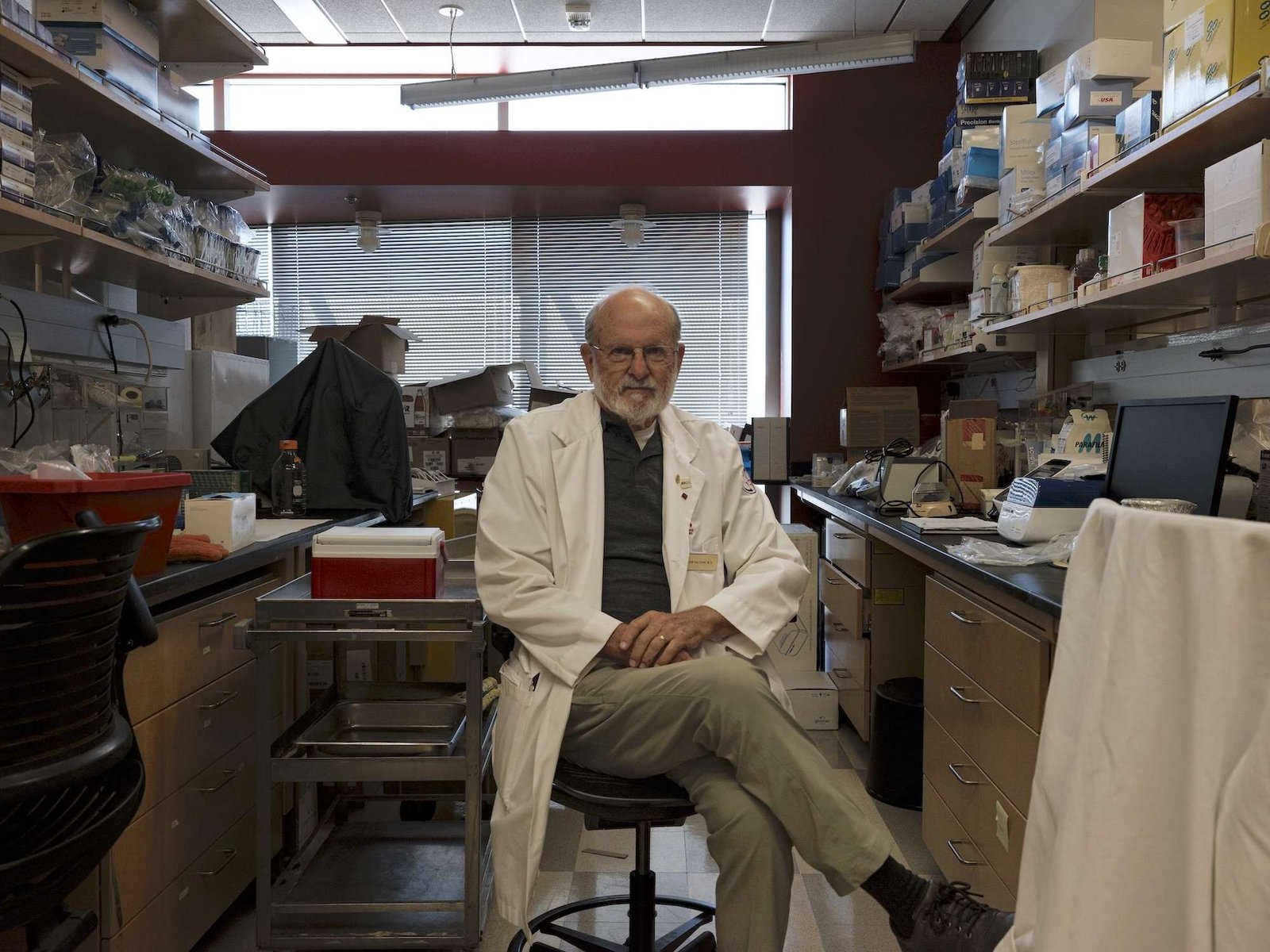 A man in a white lab coat sits in an office lab