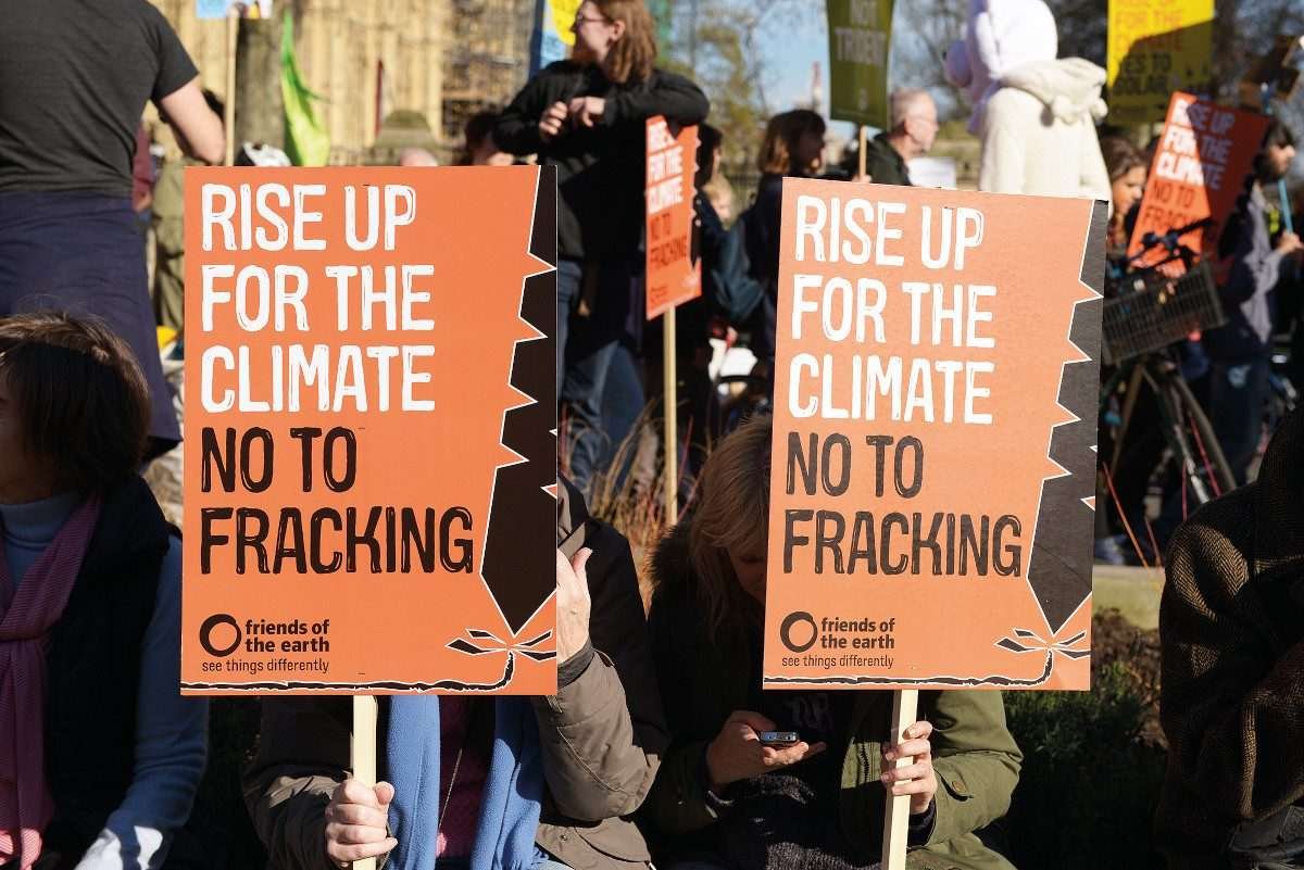 A public protest in the foreground of which appear placards bearing the slogans 'rise up for the climate' and 'no to fracking'
