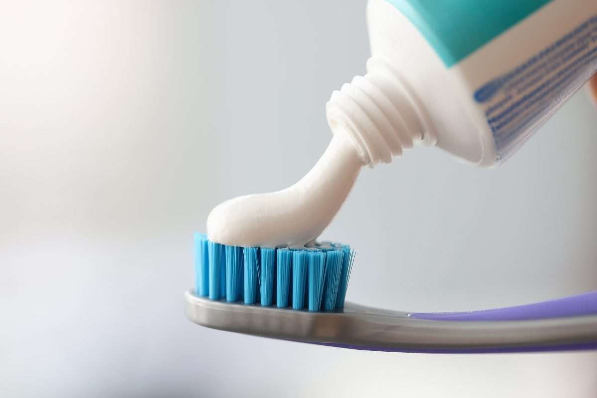 White toothpaste being squeezed onto the blue bristles of a toothbrush from a tube mostly off camera