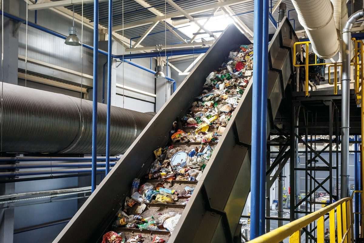 Waste cluttered on an inclined conveyor belt within a modern-looking industrial facility, a recycling facility
