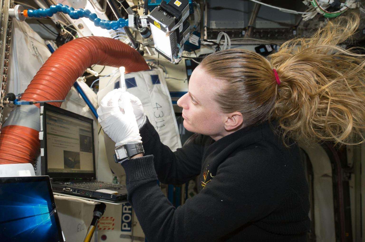 NASA astronaut Kate Rubins is looking towards the left at her hands while working on an experiment on the International Space Station.