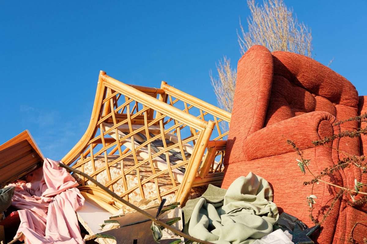 Fly-tipped furniture items piled up against blue sky background