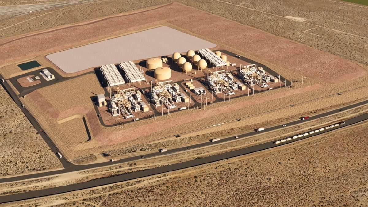 Aerial view showing complex arrangement of buildings and structures divided into rectilinear adjacent plots or segments of land, some containing cylindrical storage tanks, others containing cuboidal structures of various sizes and arrangements, all within an arid landscape and seemingly situated next to a freeway