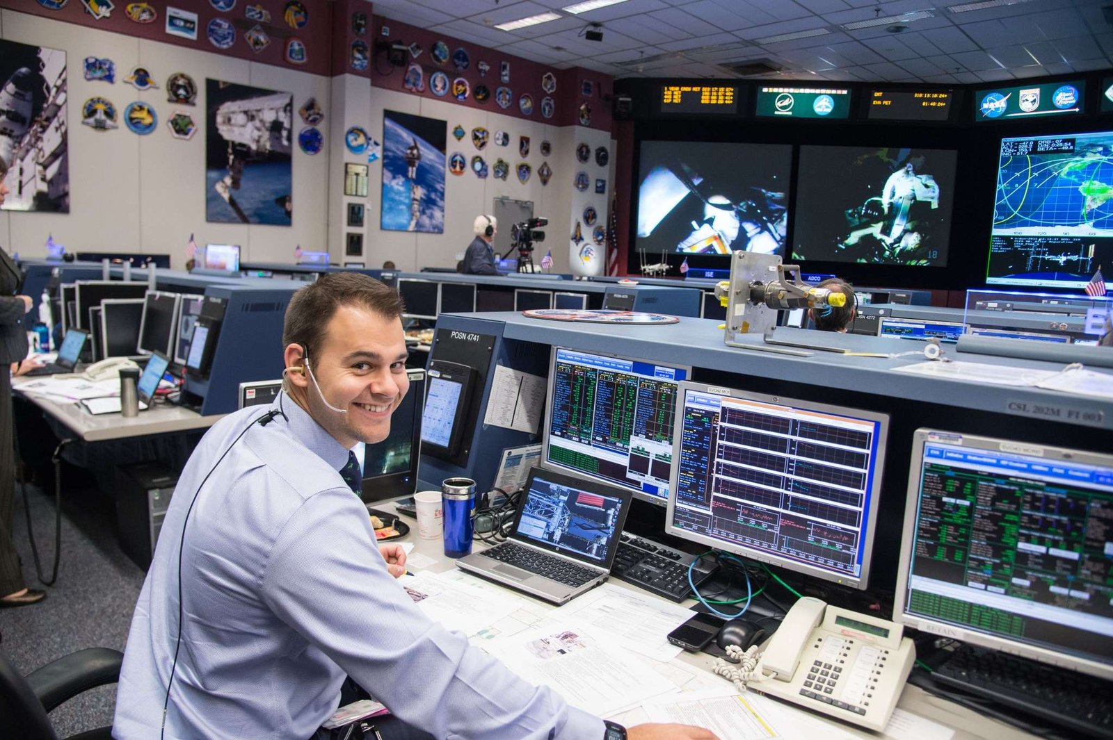 A man wearing a headset sits at a computer console in the Mission Control Center at Johnson Space Center.
