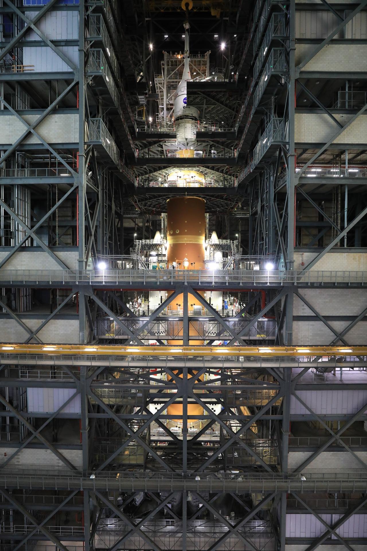 Image shows an orange core stage of the Artemis II rocket with white boosters on each side fully stacked inside the Vehicle Assembly Building at NASA's Kennedy Space Center in Florida on Saturday, Oct. 18, 2025.