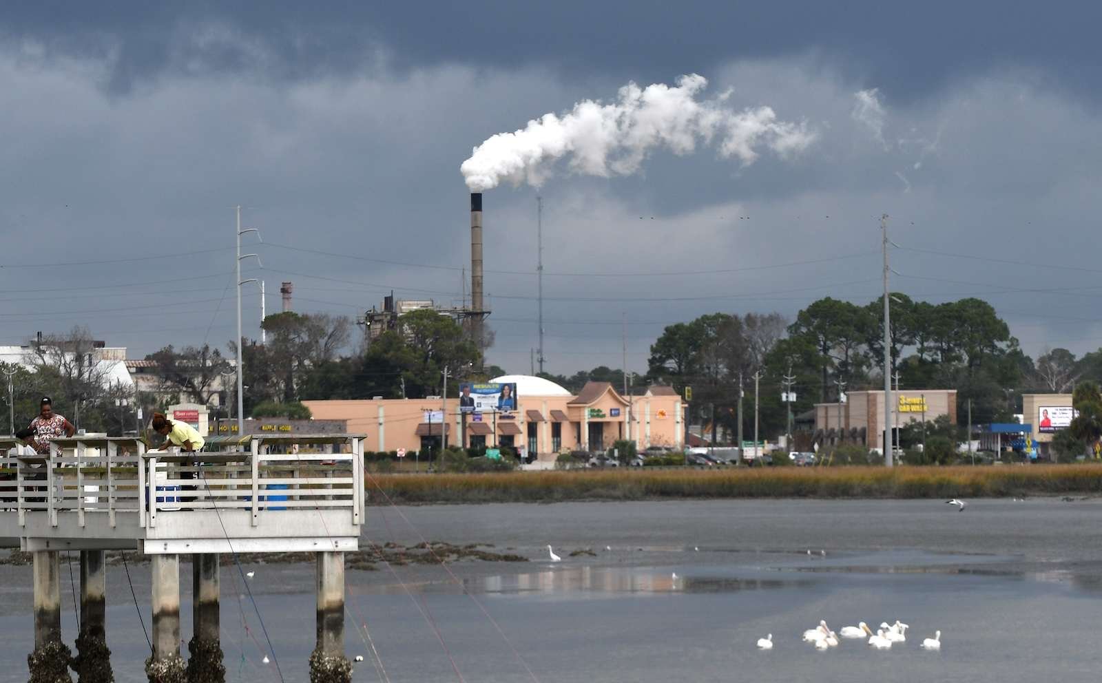 A photo shows a billowing smokestack in the background of a small waterfront town