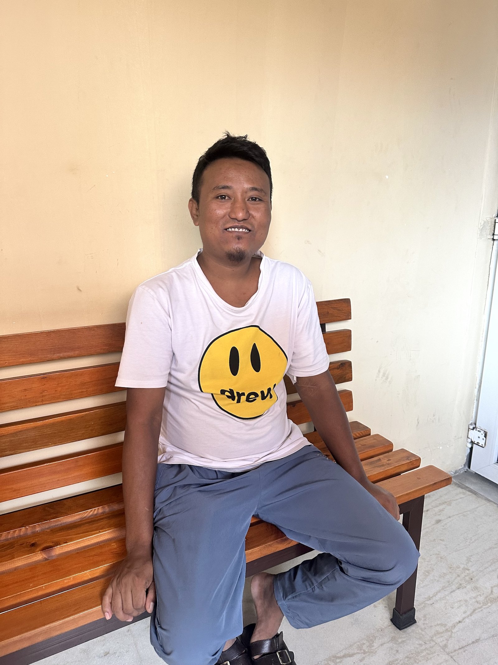 A man in a t-shirt sits on a bench outside a clinic