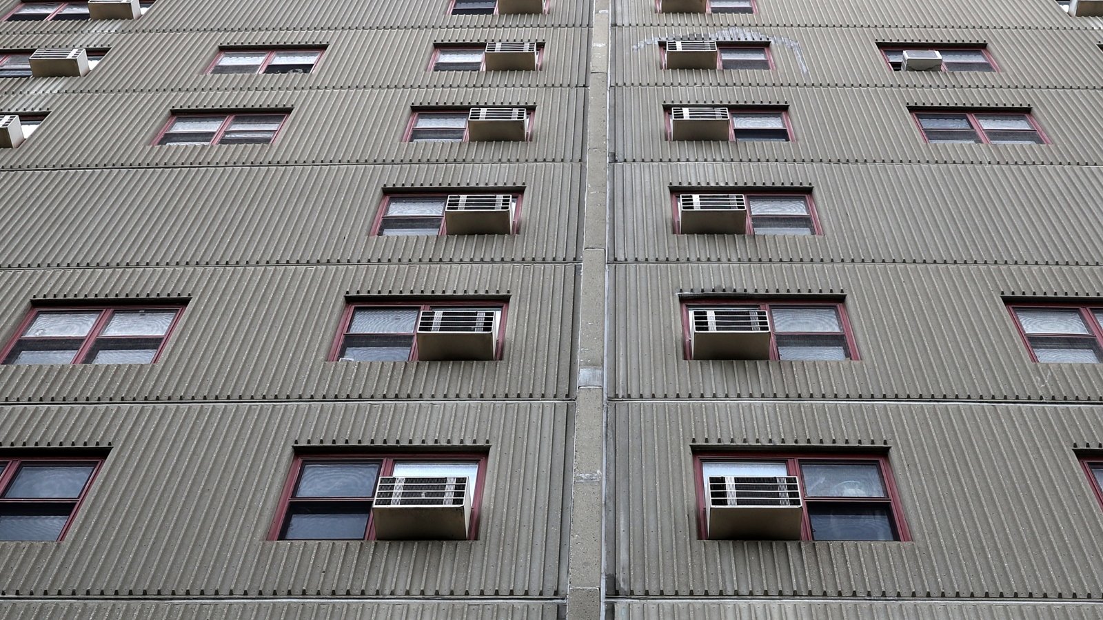 A gray building with windows each with an air conditioner embedded
