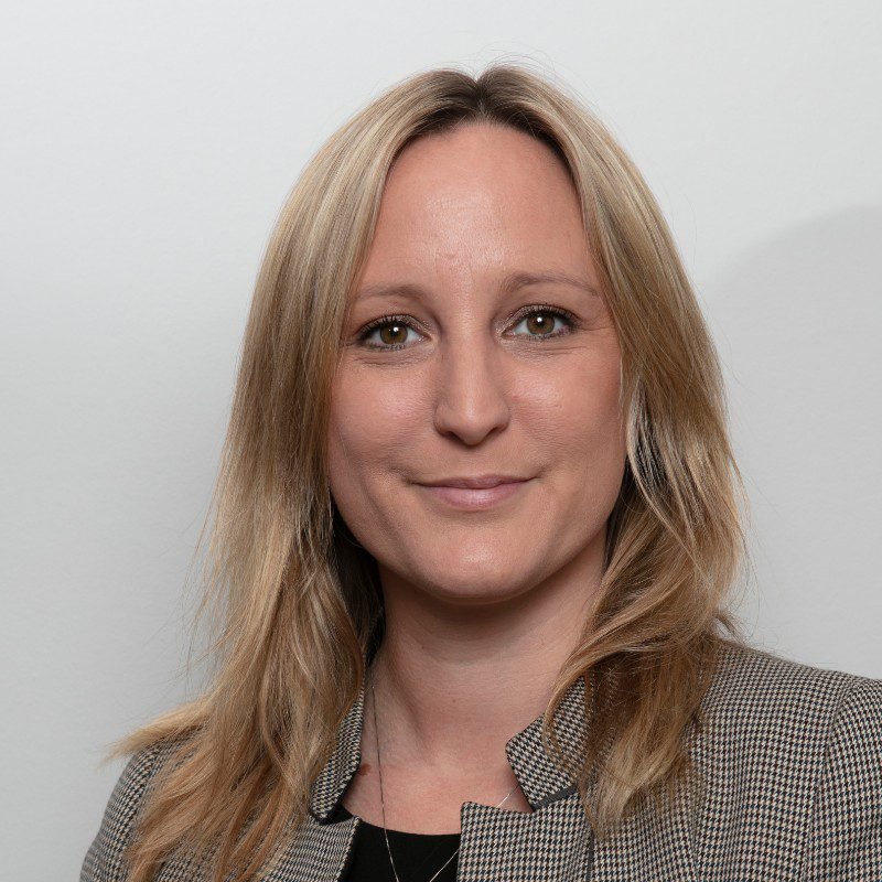 A blonde woman in business attire smiles at the camera