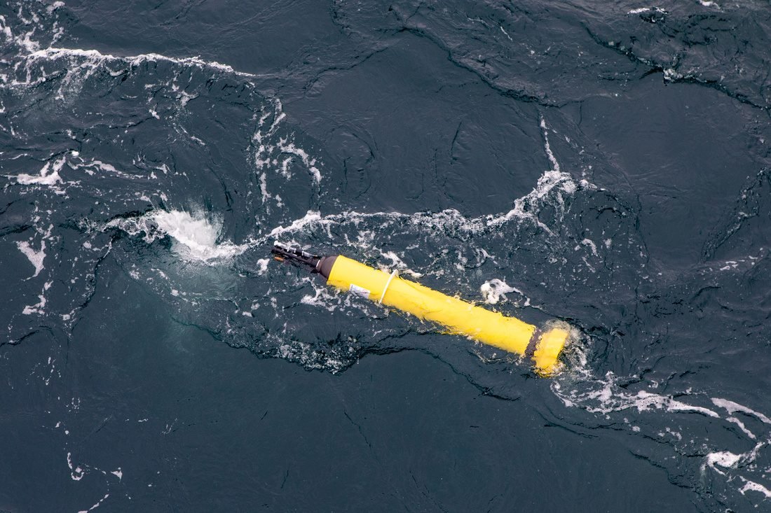 Yellow, cylindrical device - with torpedo-like shape - floats at the surface of the ocean, as seen from slightly above and to one side