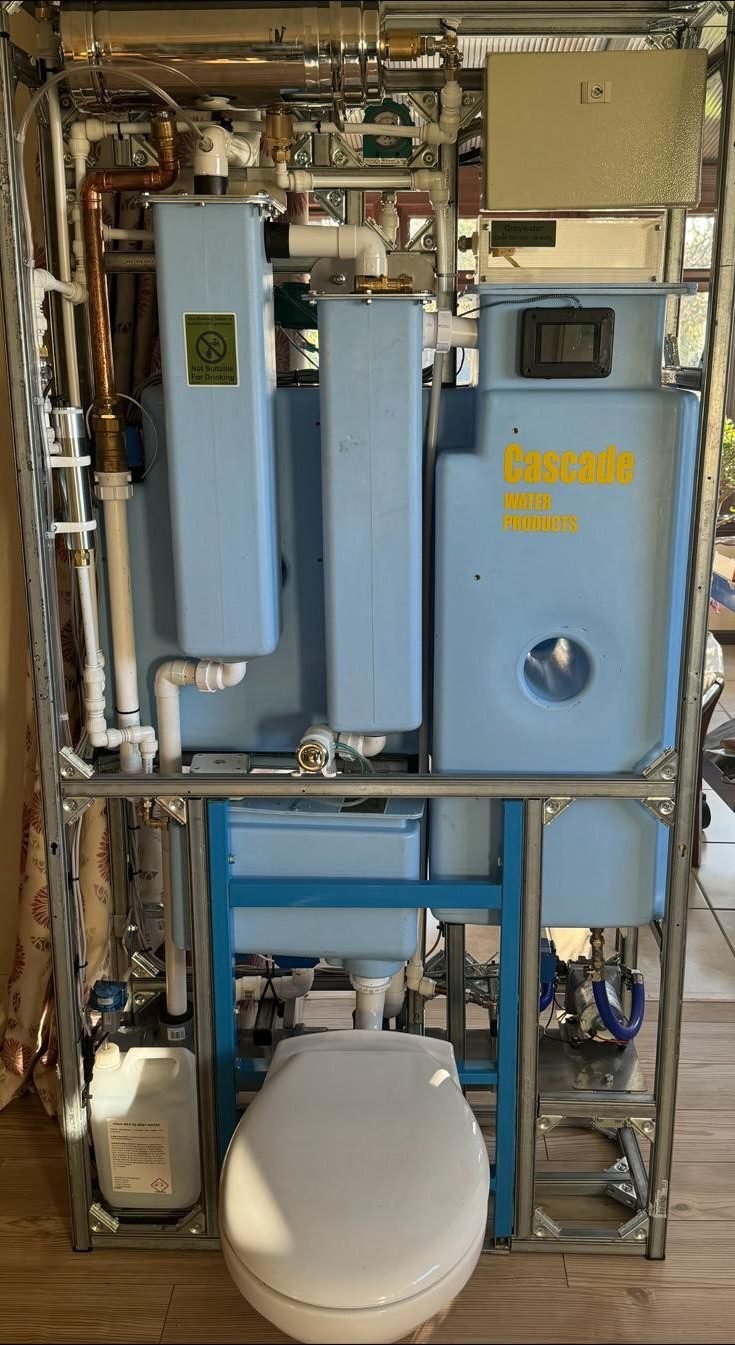 A complex assembly incorporating metallic frame, pipes, a number of blue cuboidal plastic enclosures or units and, situated in front of it all, and near the camera, a toilet cistern