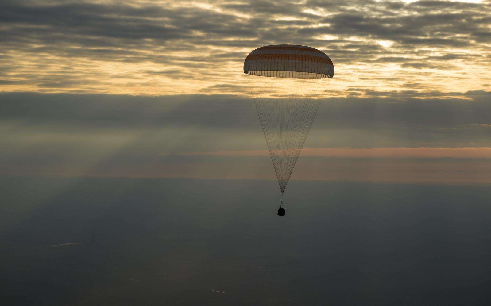 The photo features a dim horizon with the Soyuz MS-26 spacecraft as it lands by parachute.