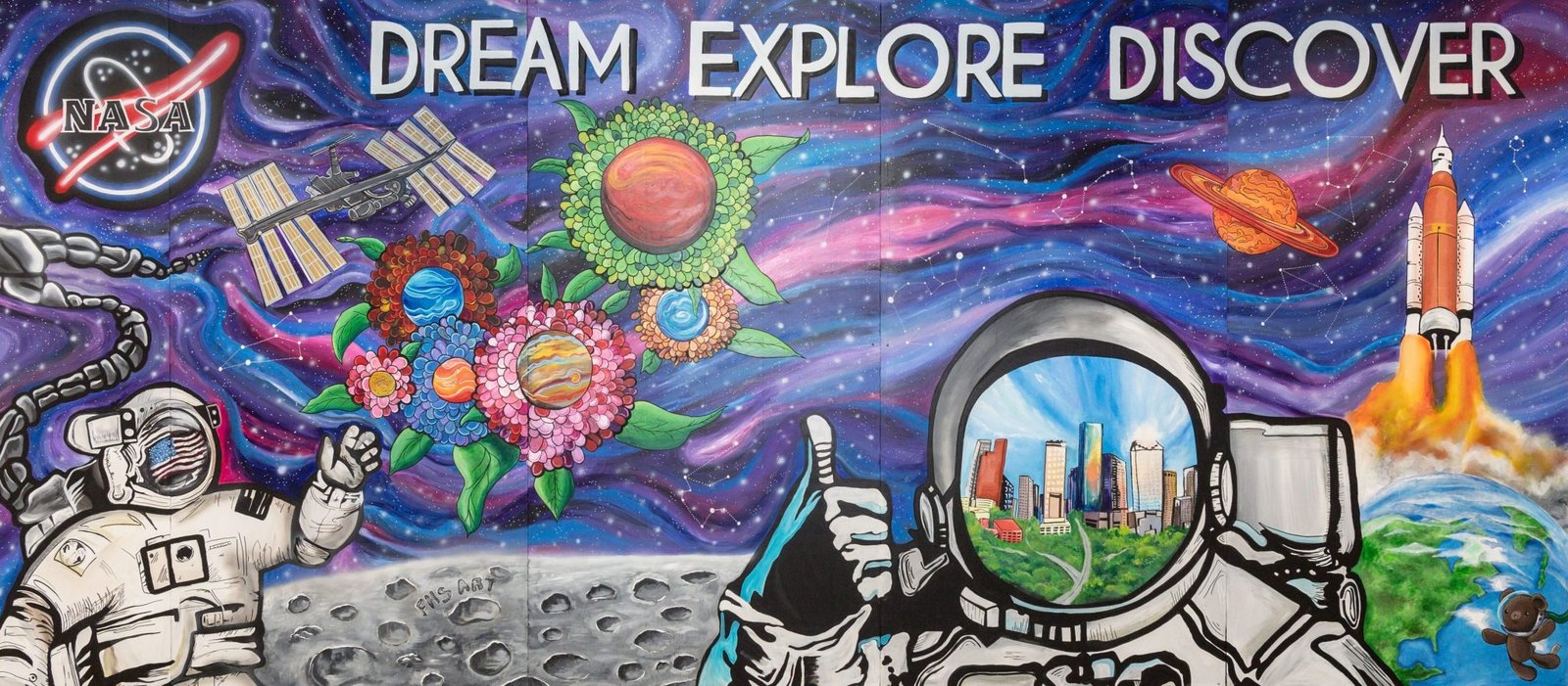 A colorful art mural featuring two astronauts on a lunar landscape with the Earth and a rocket in the background. The NASA meatball insignia is in the top left corner.