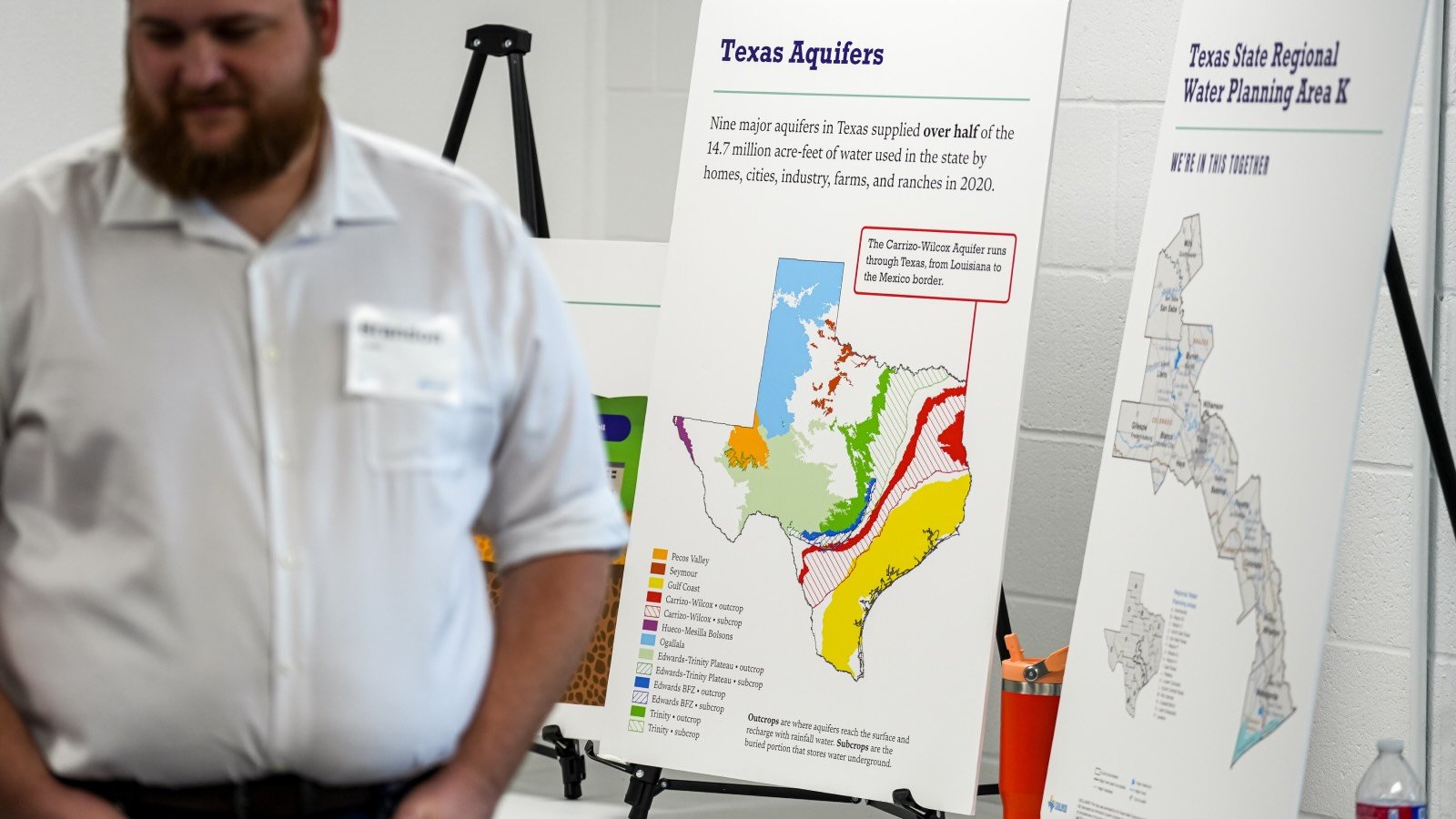 A man stands in front of two posterboards, one showing a map Texas with its aquifers displayed in color