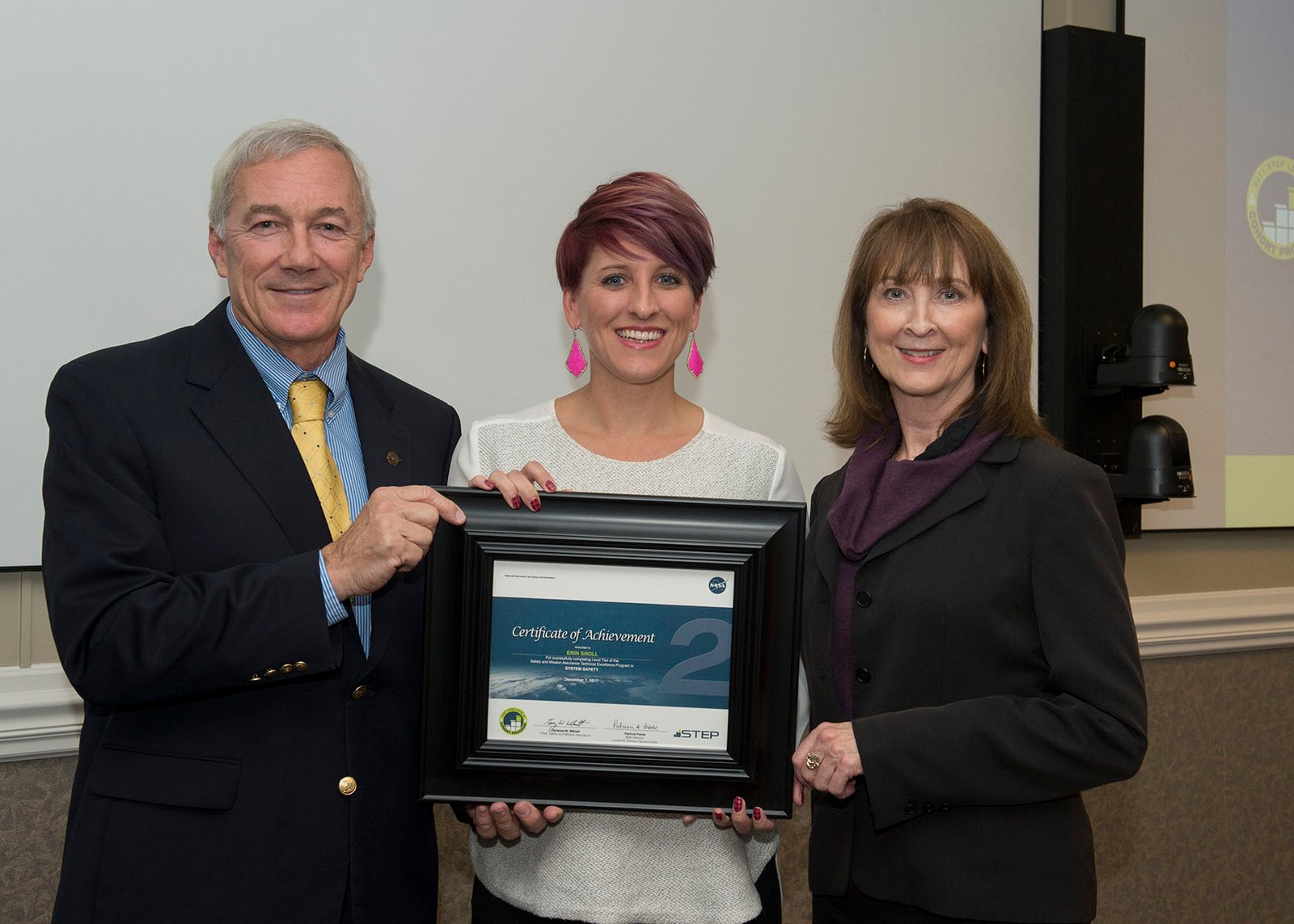 A woman receives a framed honor from two colleagues, a man and a woman.