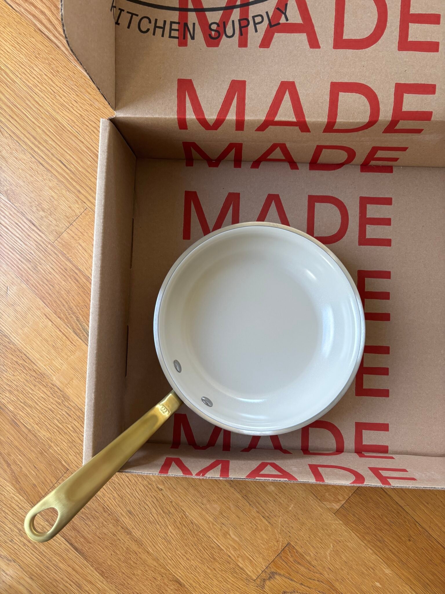 A small white saucepan with a gold handle sits inside an open cardboard box with "MADE" printed in large red letters.
