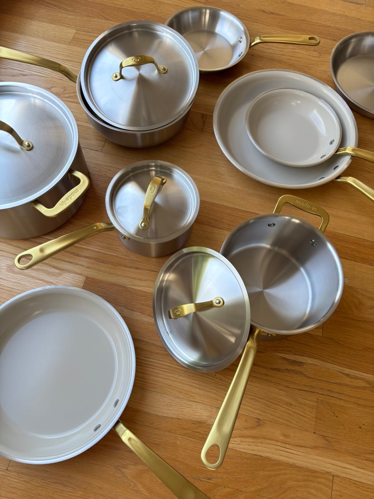 A set of stainless steel pots and pans with gold handles and lids arranged on a wooden floor.