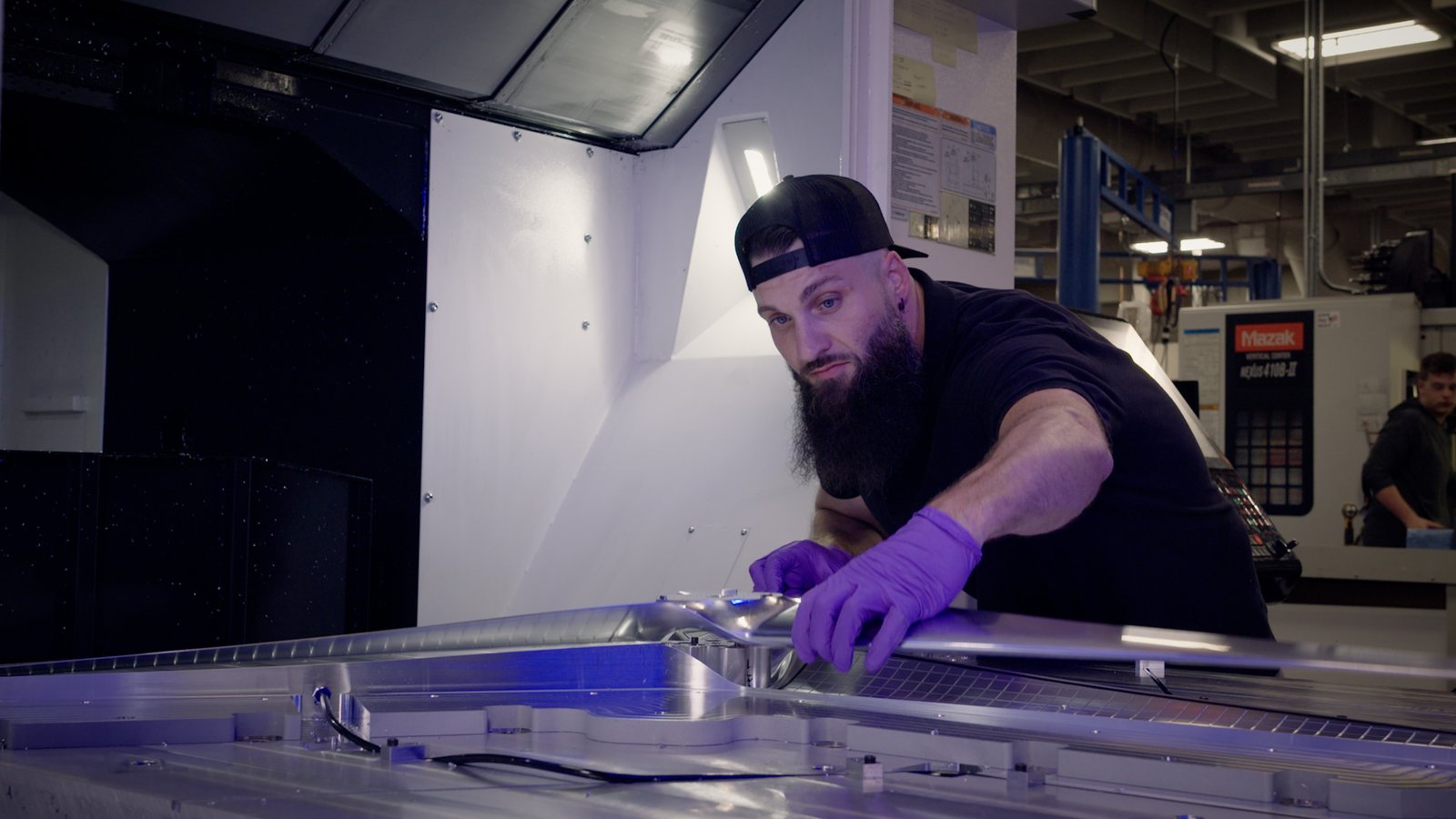 A man wearing dark clothes and purple gloves works on a silver rotor on a table.