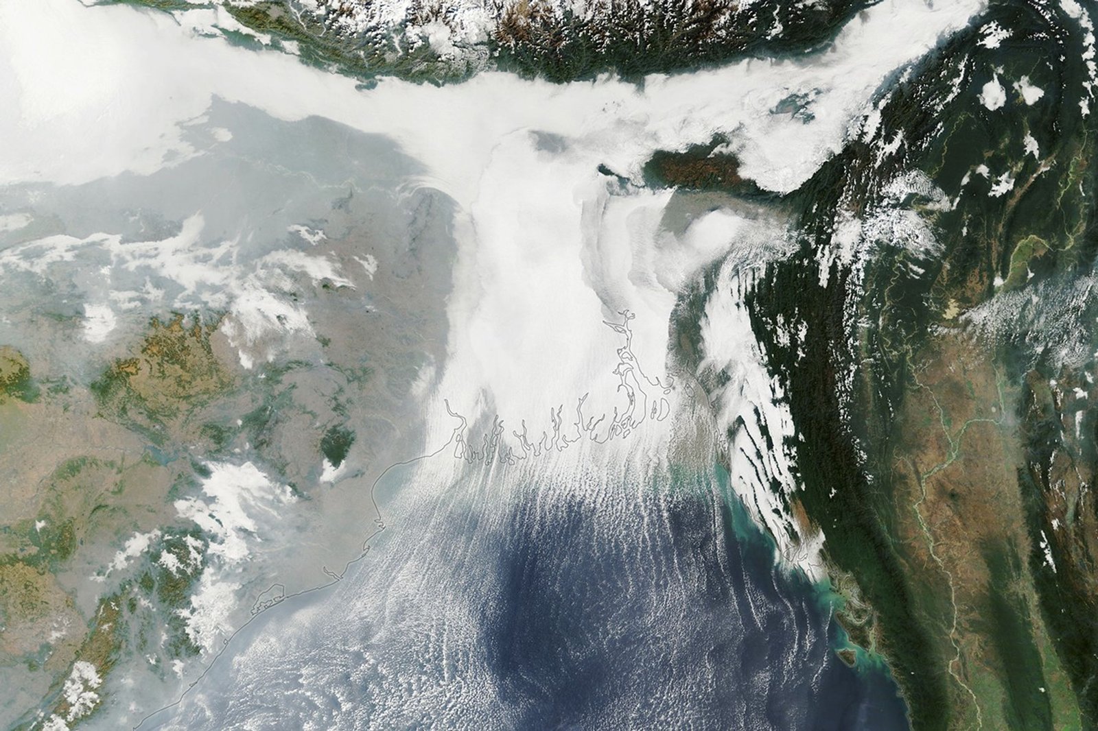 A satellite image of the Ganges Delta shows a T-shaped area of low white clouds. At the bottom, clouds extend over the blue waters of the Bay of Bengal in parallel rows.