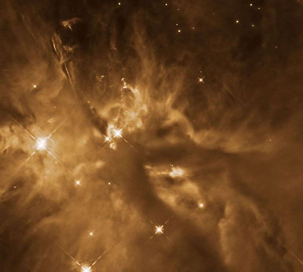 A tumultuous orange cloud of gas and dust is laced with areas of dark dust and scattered with bright stars.