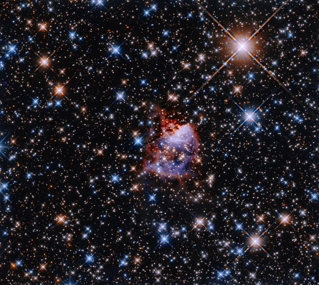A small, bluish cloud edged in red gas is in the center of a field thick with multicolored stars.