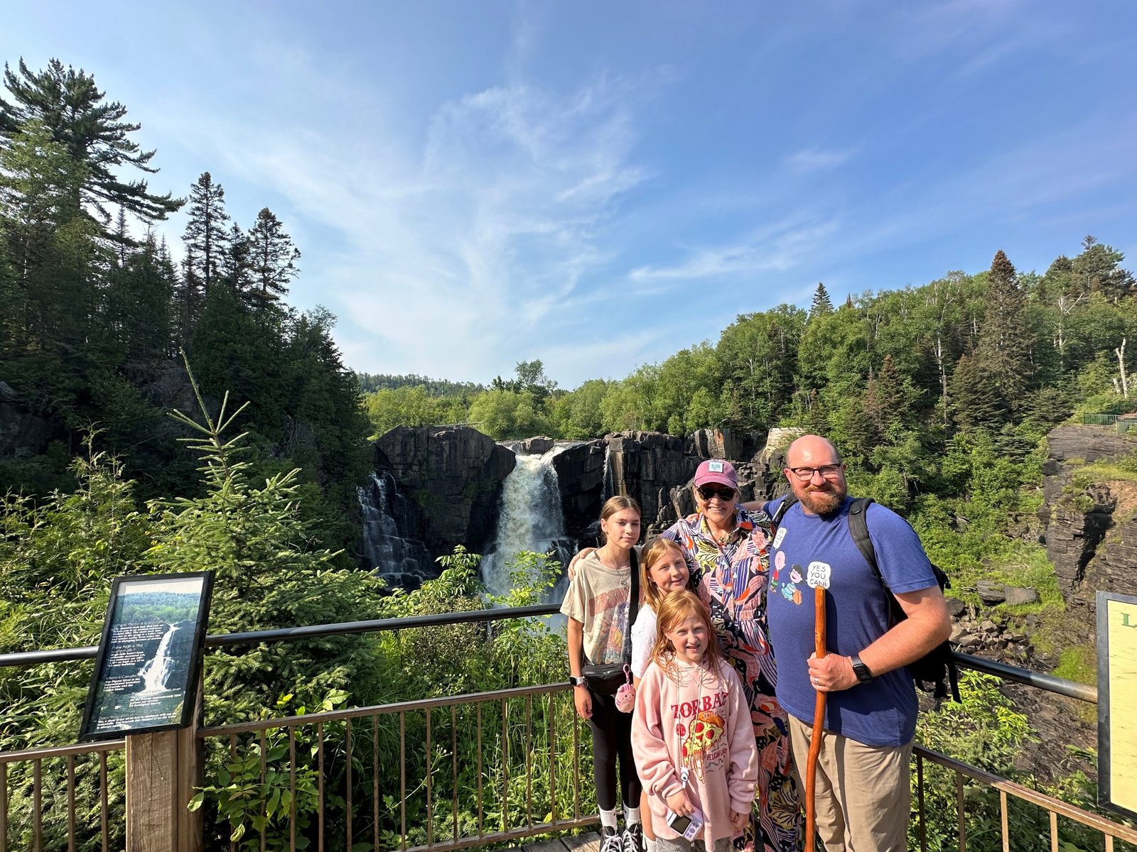 A family of four stands in front of nature and a waterfall.