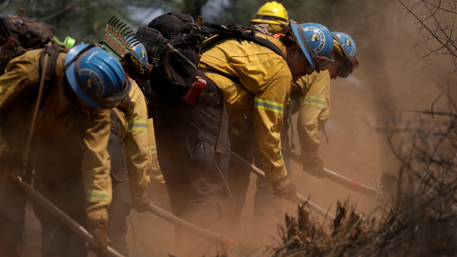 Photo of people in yellow jackets and hard-hats working with shovels in smoky conditions