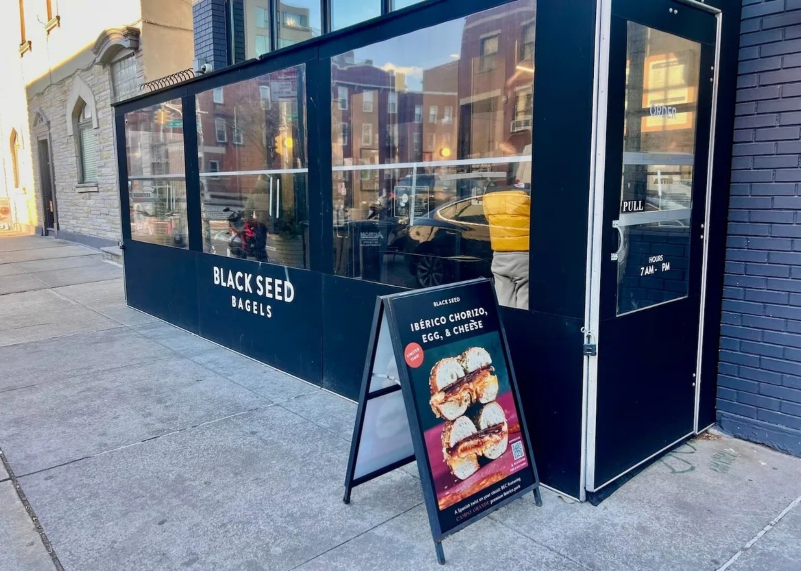 A black storefront with 'Black Seed Bagels' in white lettering and a sandwich board on the sidewalk