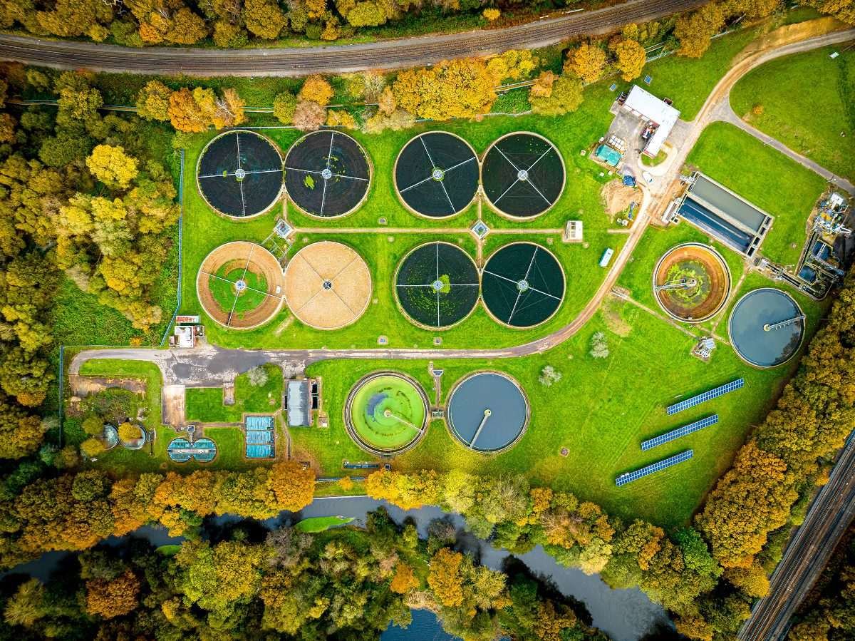 Circular clarification tanks of a water treatment site, set within a green and rural lanscape, seen from directly above, at a significant height