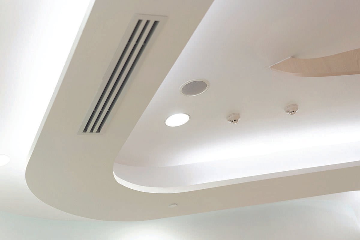 A white plastic extrusion from the surface of a white ceiling, the surface of which is marked by a series of long, thin vents