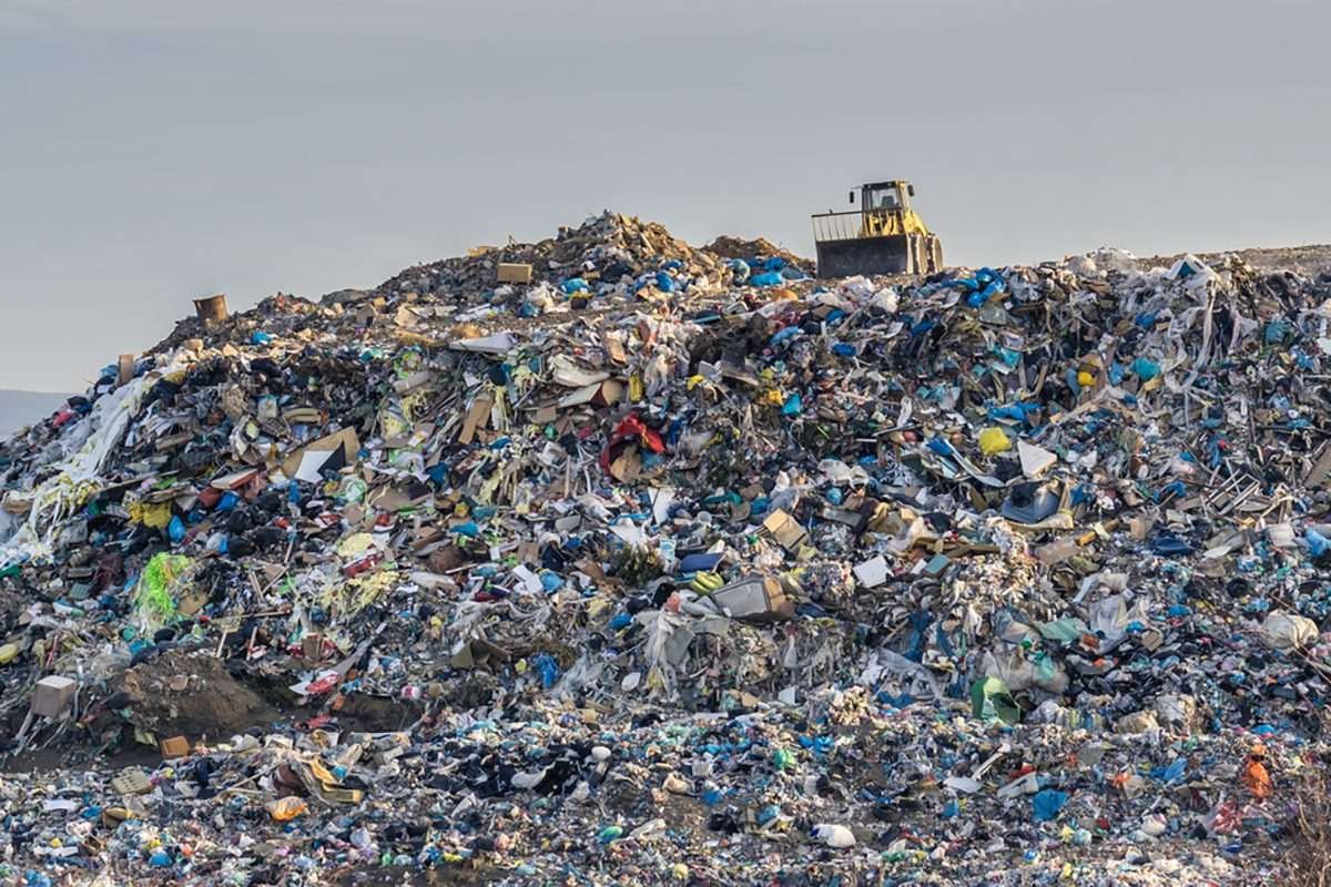 A yellow utility vehicle is visible in the distance against the skyline of a large landfill
