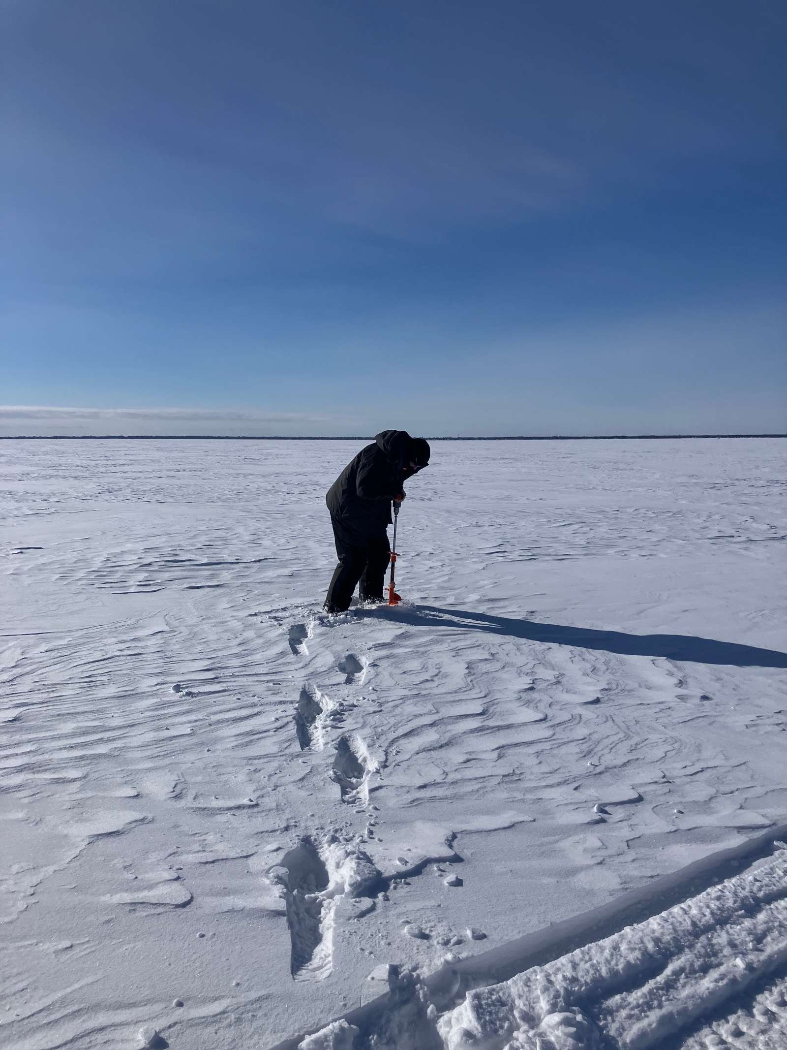 A man uses an auger to drill into ice