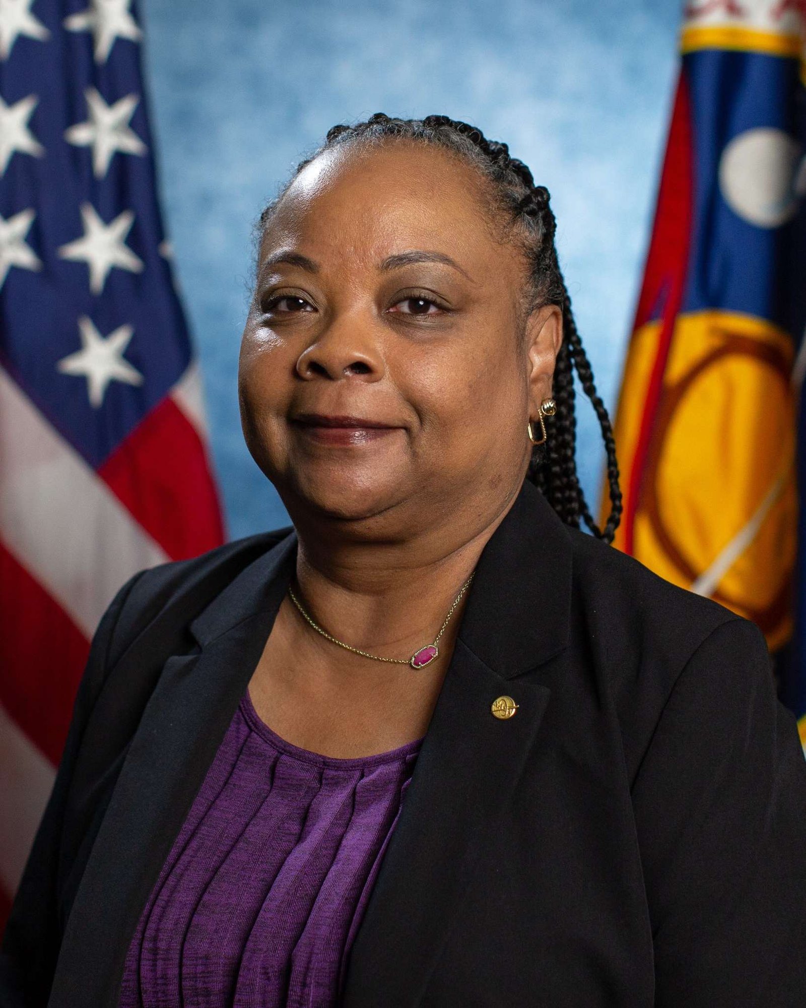 A Black woman wearing a purple blouse and black blazer sits in front of the American flag and the NASA flag.