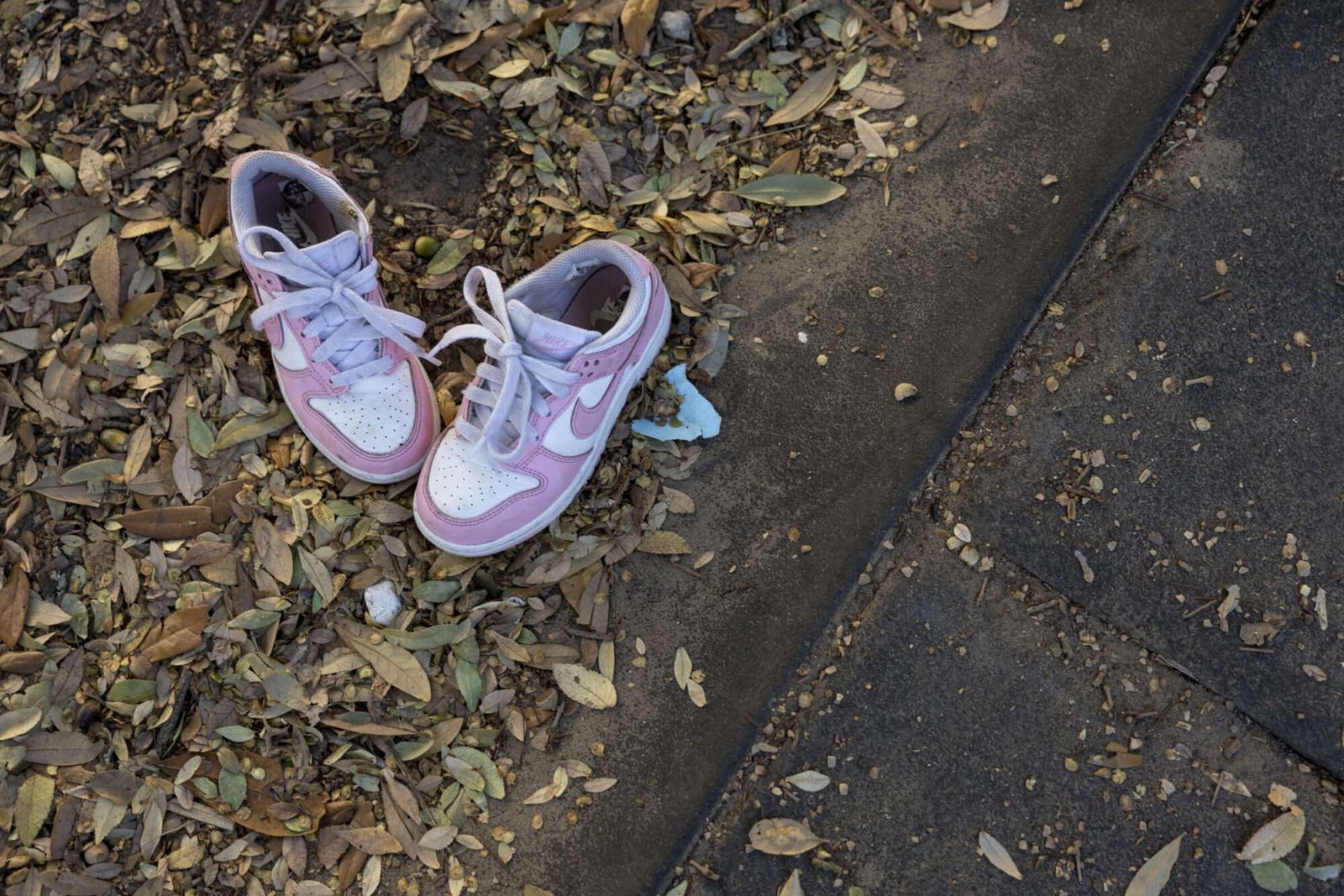 Two pink child size sneakers are seen on a sidewalk