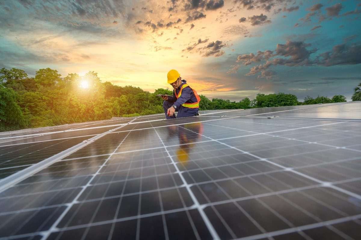 Solar panels on an upward incline - possibly a rooftop - with installation engineer in hard hat visible within the scene