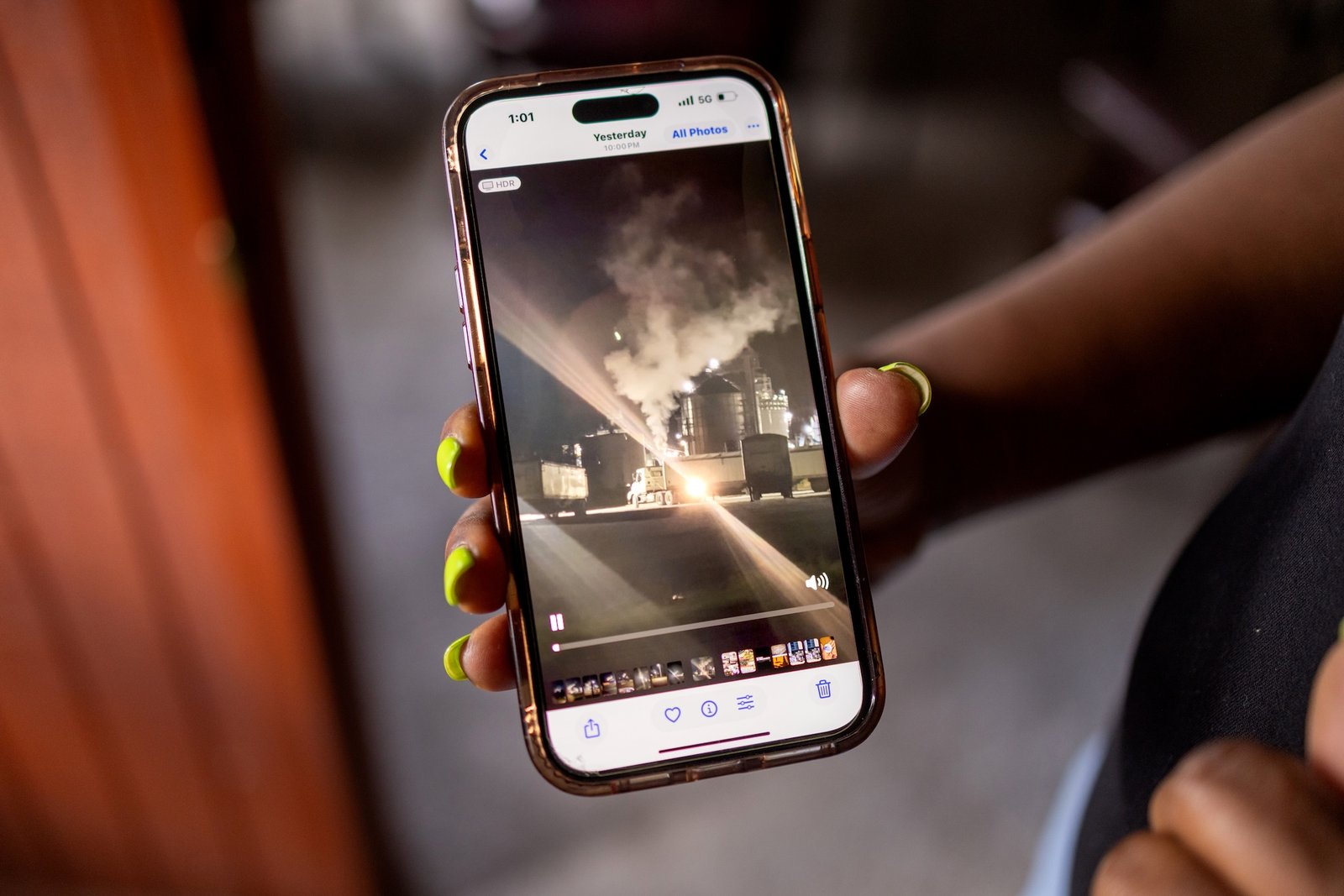 A woman holds a phone showing pollution from an industrial plant at night