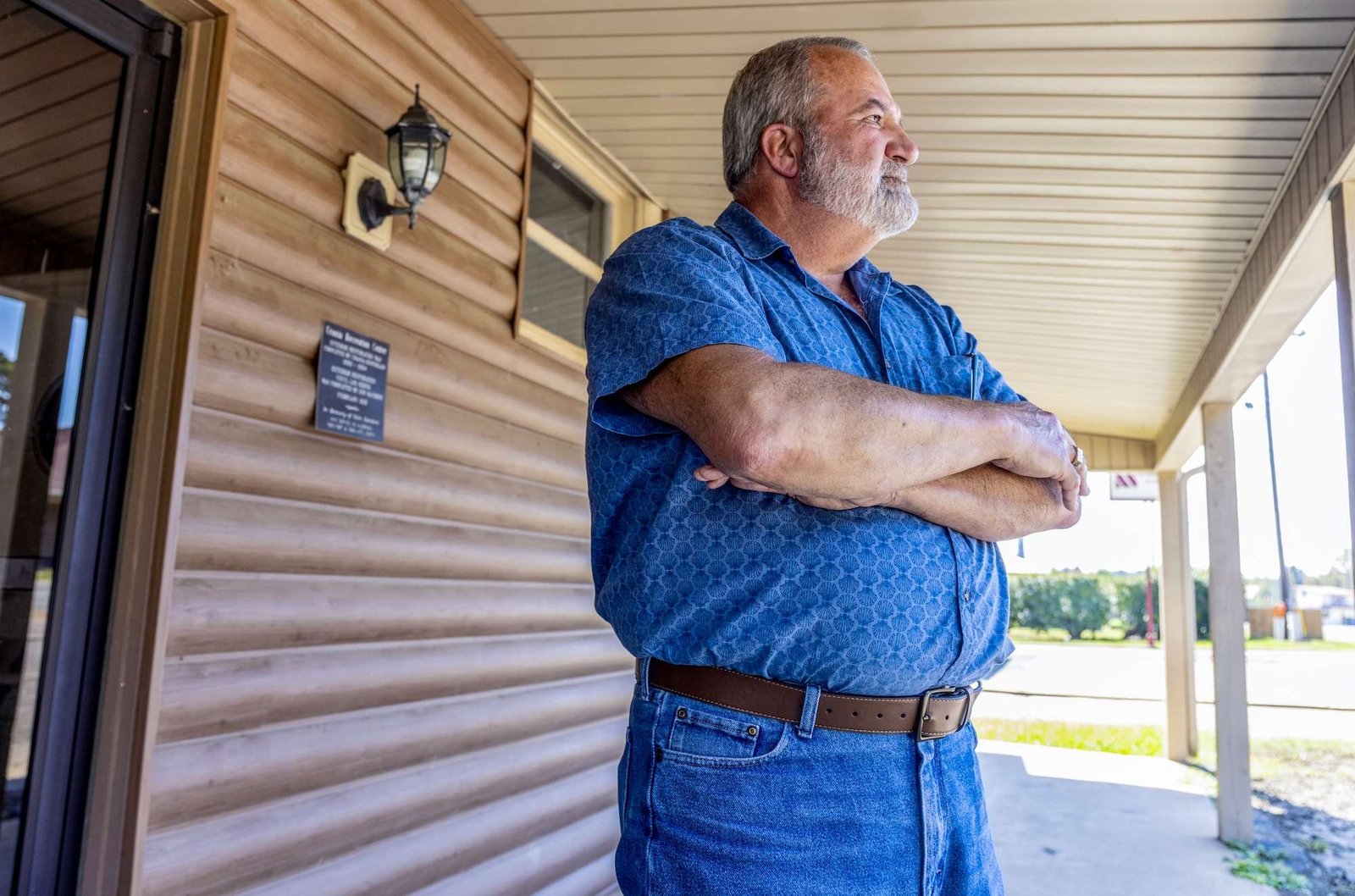 A man in a blue shirt stands on a porch of a building and looks off into the distance
