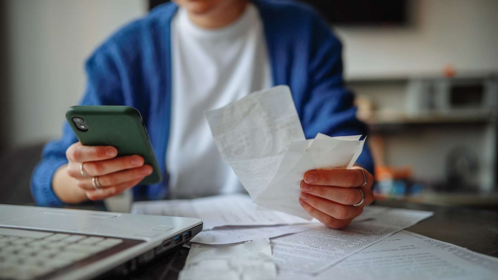 A woman pays bills at the kitchen table.