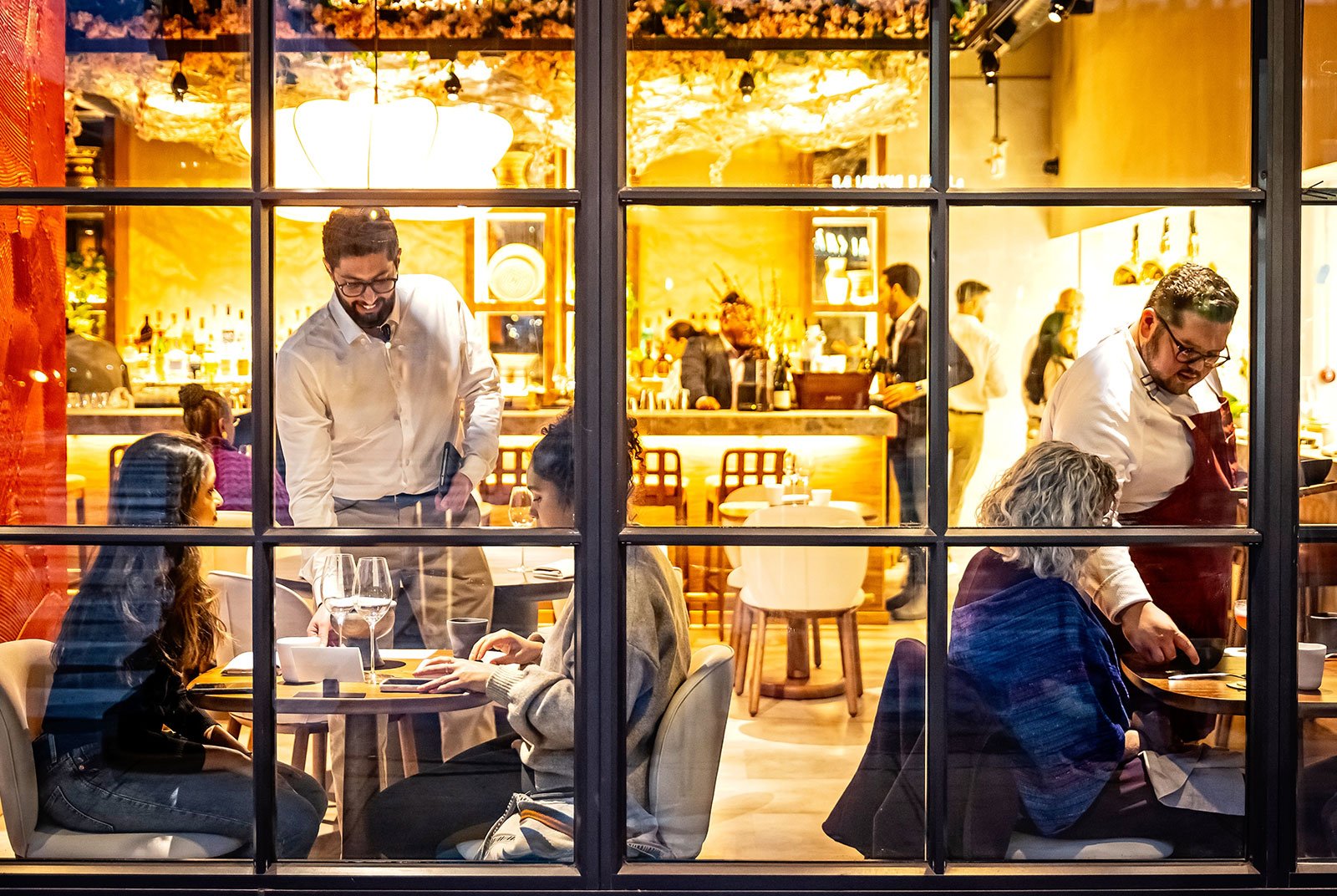 View of diners inside warmly-lit restaurant through window panes
