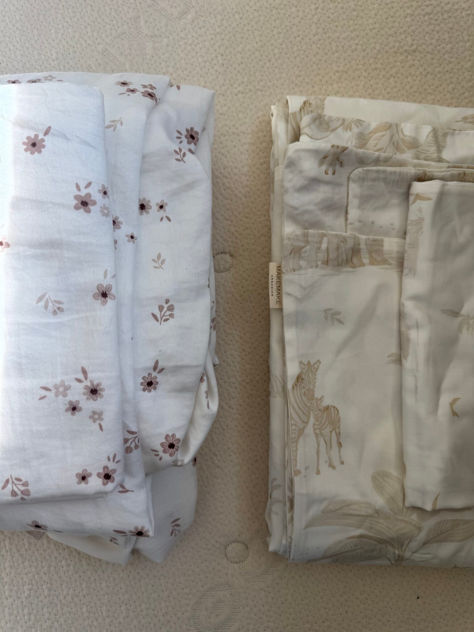 Two folded stacks of bed sheets on a textured surface; the left has a small brown floral pattern, the right features a light animal and plant design.