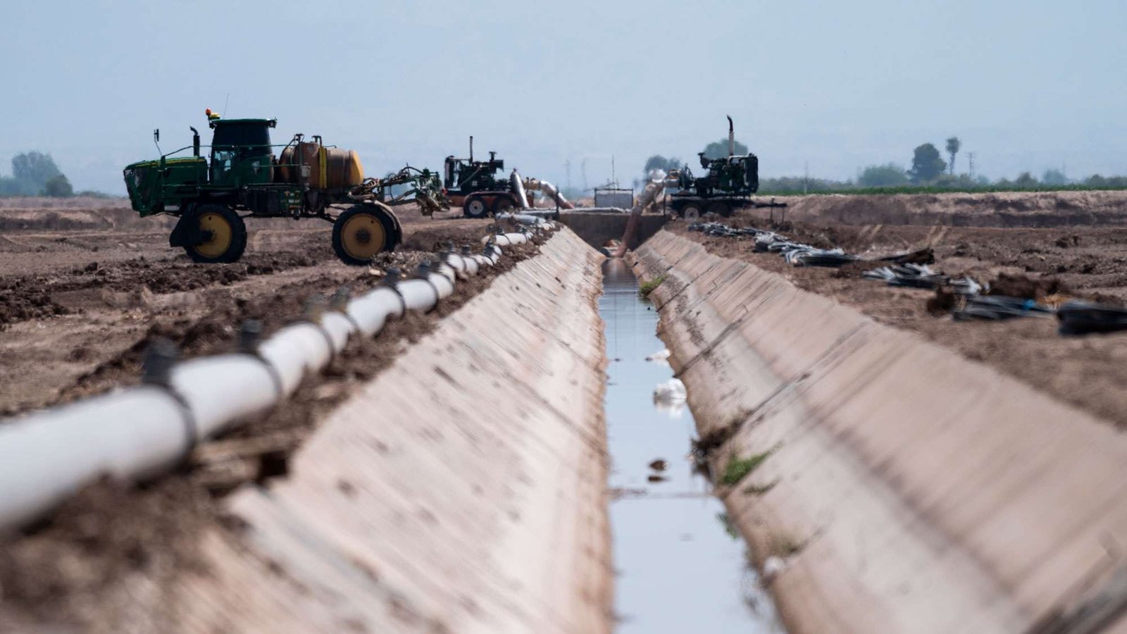 Low angle of an irrigation canal with farm equipment on either side, and drought-ridden land