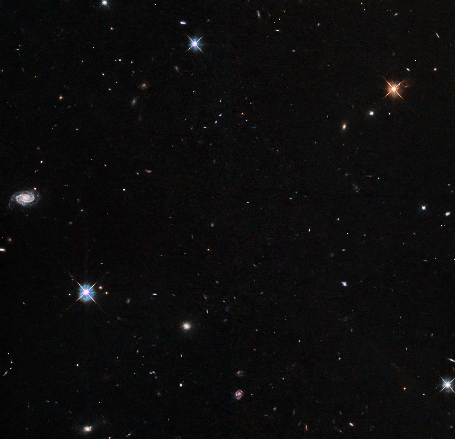 Several bright stars and many background galaxies are visible against a black background.