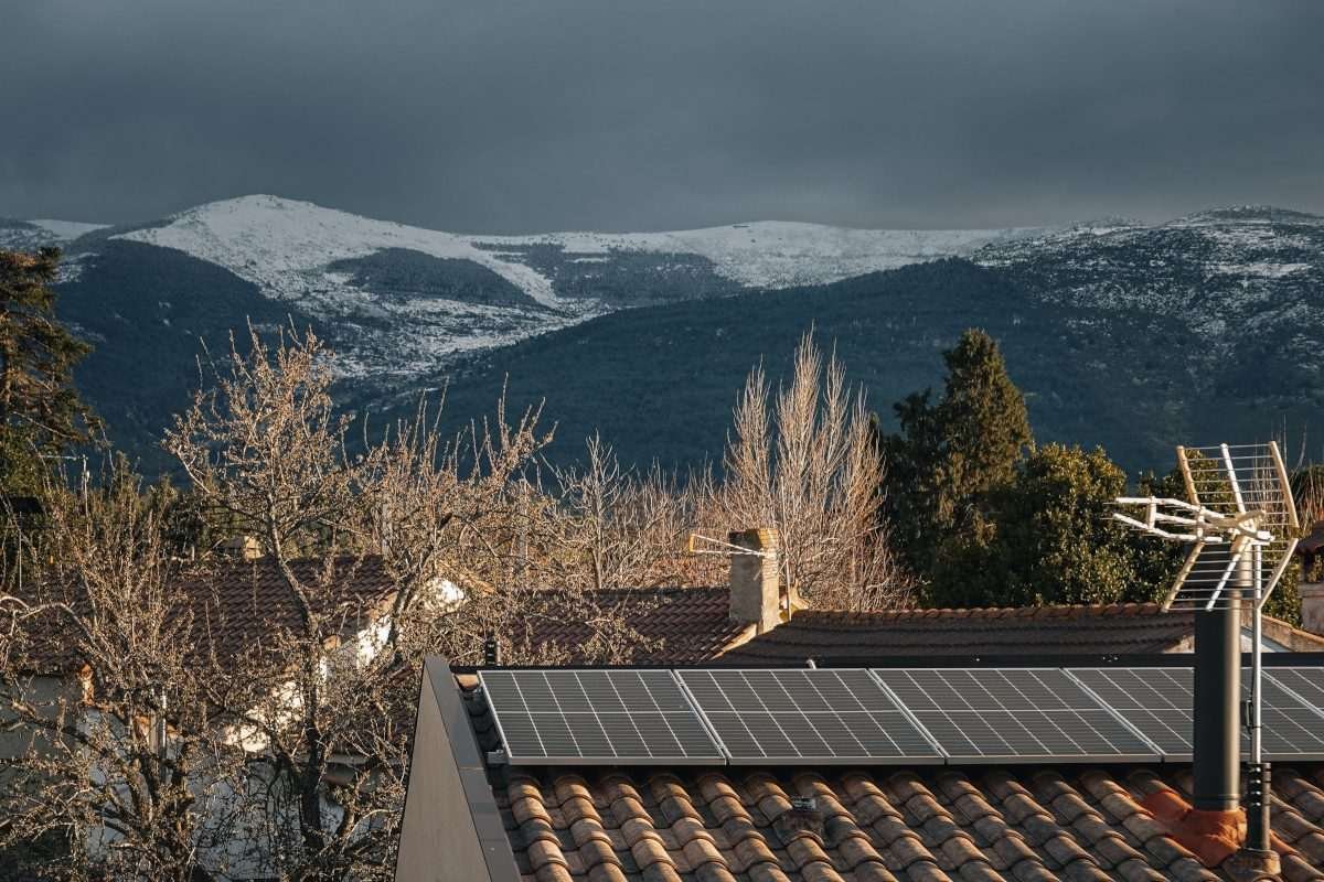 a rooftop solar installation in a village with snowy mountains visible in the distance