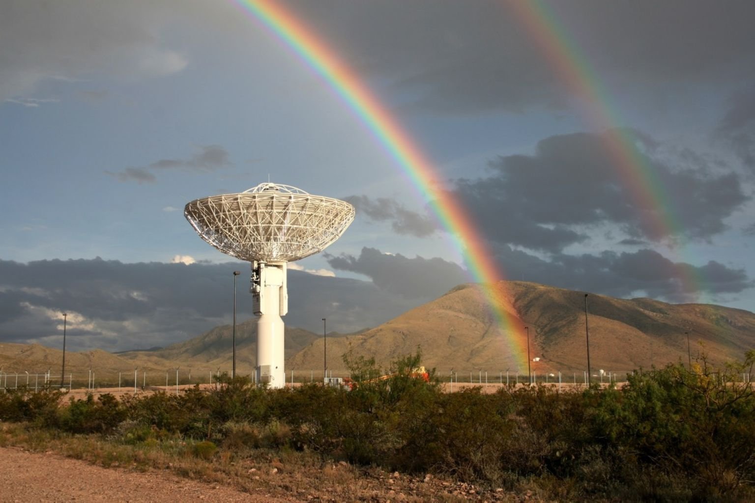 A double rainbow arcs above a Near Space Network antenna pointed to the sky.