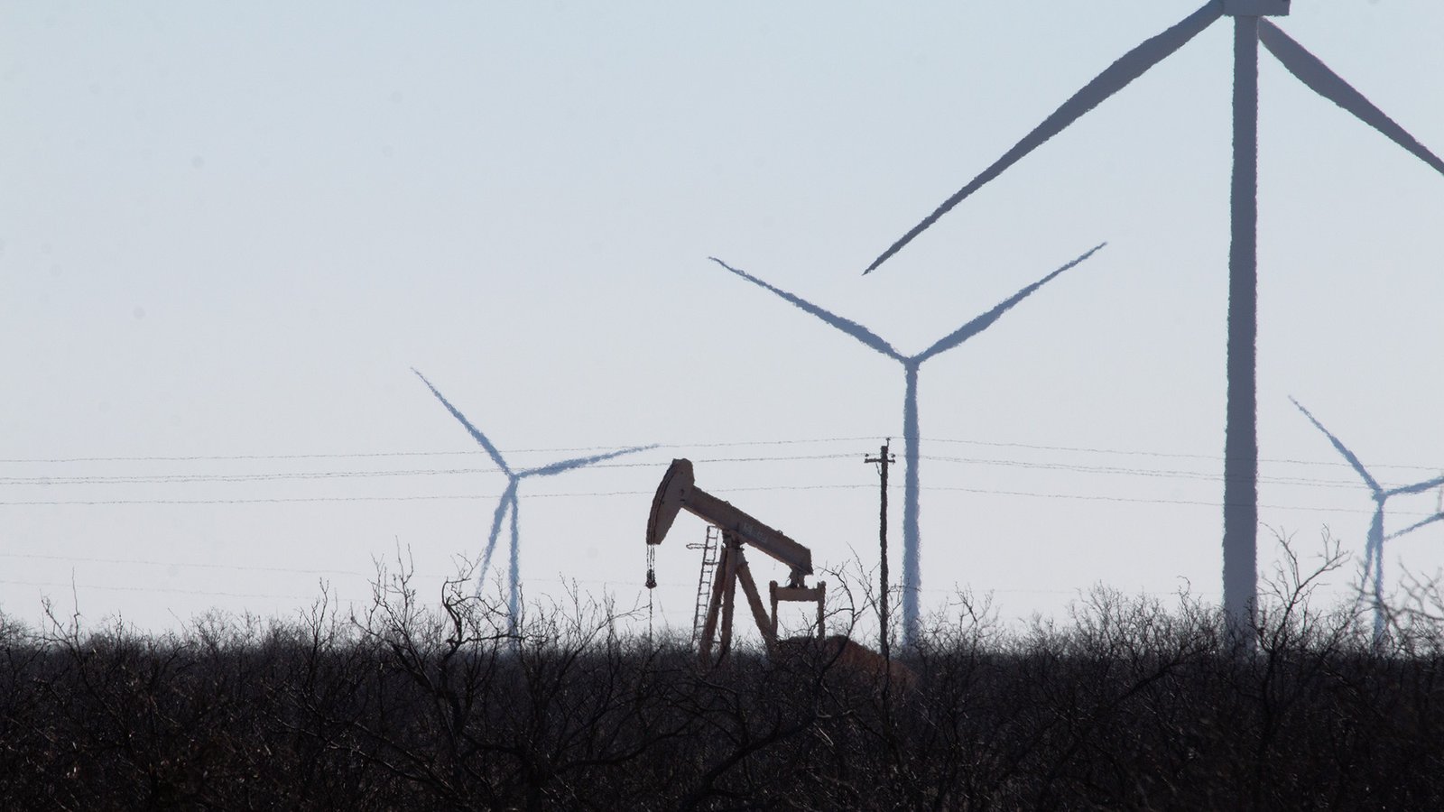 An oil pumpjack is seen in the same field as several wind turbines