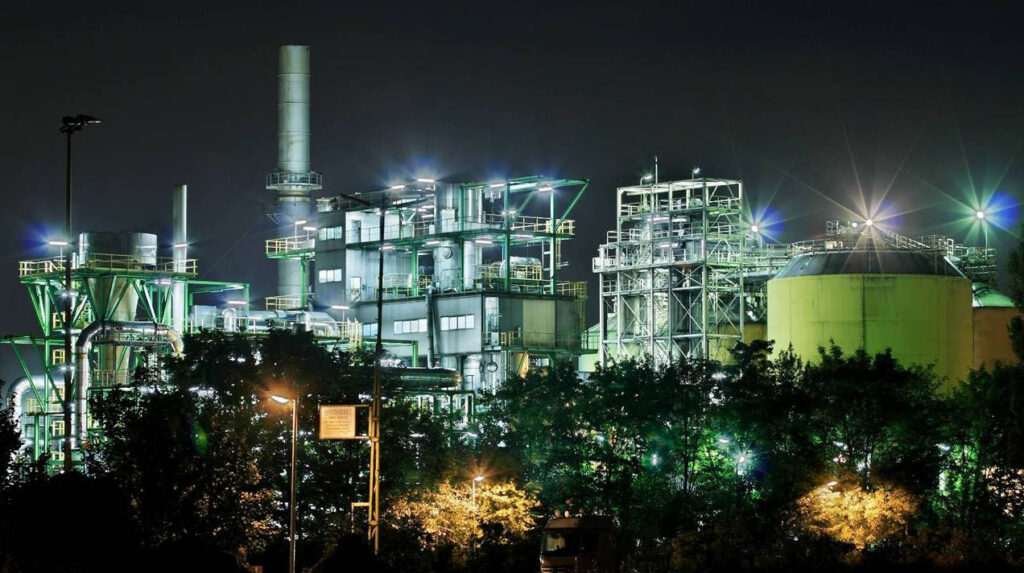 A Birla Carbon plant at night-time, with a range of lights and buildings alongside a tall chimney.