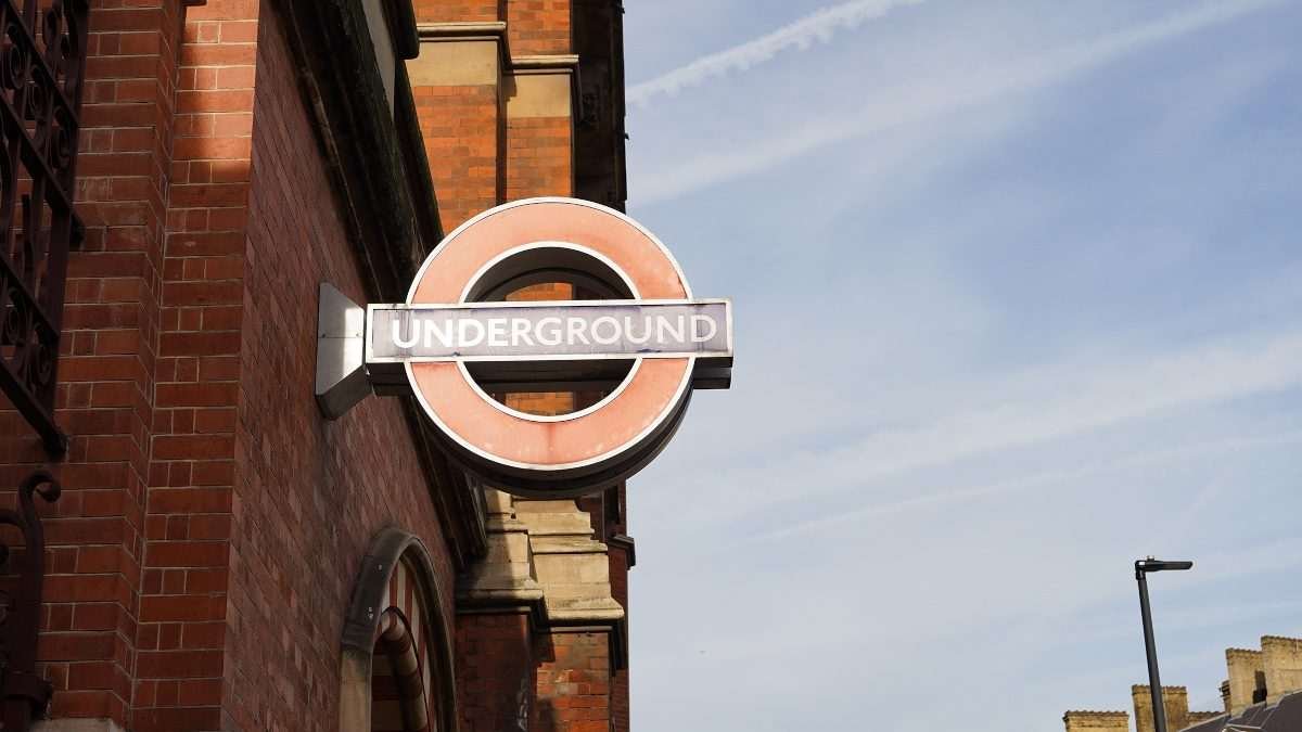 Overhead London Underground sign protrudes from the red brick wall of a building with blue-ish sky visible as a backdrop