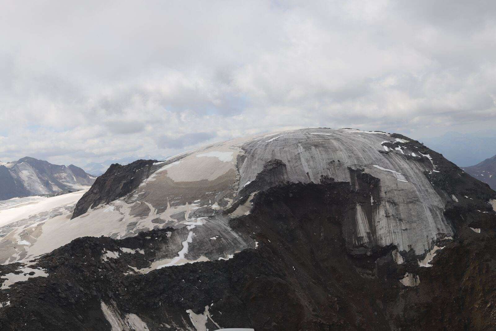 A soot-colored mountainside where an icy glacier is receding