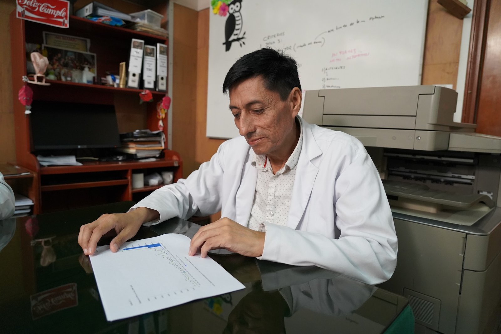 A man in a white doctor's coat looks at a piece of paper in a medical office